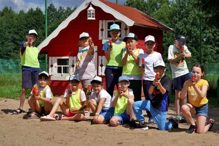 grupa dzieci a za nimi drewniany domek